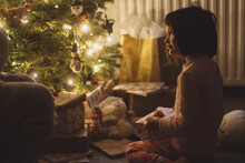 A Young Girl In Her Pajamas Early On Christmas Morning, Beginning To Open Presents