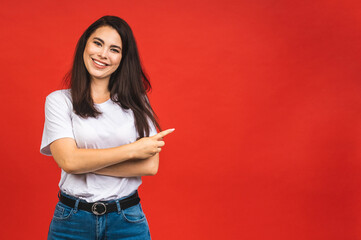 Wall Mural - People, youth, leisure and lifestyle concept. Fashionable beautiful young amazed Caucasian young female student wearing stylish clothing laughing, pointing finger away. Isolated over red background.