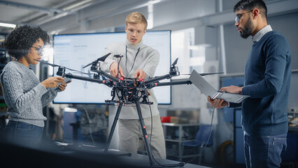 Leinwandbilder - Black Male Engineer Coding on Laptop While Programming Drone with his Colleagues In the Factory Laboratory. Scientific Research, Design, Operation and Performance of Machine Mechanism Concept.