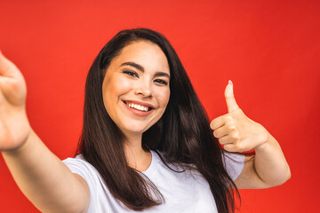 Canvas Print - Portrait of pretty young happy woman making selfie on smartphone, isolated over red background.