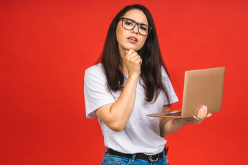 Canvas Print - OMG! I'm shocked! Portrait of a shocked young beautiful business woman holding laptop computer isolated over red background.