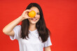 Young beautiful brunette woman holding orange fruit isolated over red background.