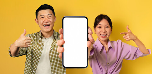 Poster - Smiling Asian Man And Woman Demonstrating Empty Smartphone With Big White Screen