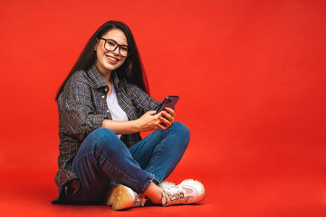 Canvas Print - Business concept. Portrait of happy brunette woman in casual sitting on floor in lotus pose and using mobile phone isolated over red background.