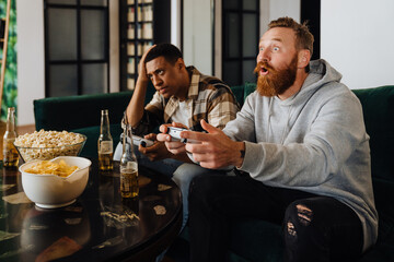 Wall Mural - Excited white ginger man playing video game with his friend and winning