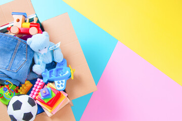 Wall Mural - Donations box with kid toys, books, clothing for charity on colorful yellow, pink, light blue background. Top view