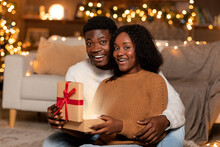Surprised Glad Millennial African American Lady And Man Opens Box With Gift, Light In Cozy Living Room