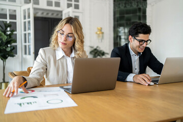 Finance experts a man and a woman work together in the office on an online project. Use laptops