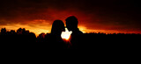 Fototapeta Łazienka - Silhouette of a young couple in love face to face against the background of the orange sky during sunset.
