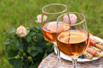 Canvas Print - Glasses of delicious rose wine and food on picnic basket outdoors, closeup