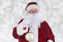 Santa Claus Holding A Large Gold Pocket Watch, With The Time Showing Almost Midnight, Bokeh Background With Snow Effect.