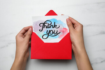 Wall Mural - Woman holding envelope and card with phrase Thank you at white marble table, top view