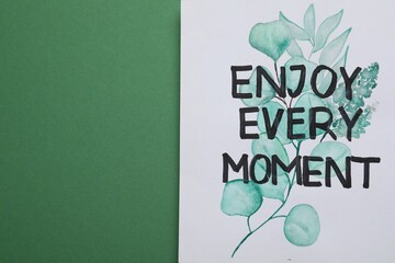 Wall Mural - Card with phrase Enjoy Every Moment on green background, top view. Space for text