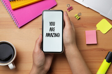 Wall Mural - Closeup of woman holding smartphone with phrase You Are Amazing on screen, top view