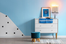 Plate With Cookies, Torah, Dreidels, Menorah And Picture On Chest Of Drawers Near Blue Wall