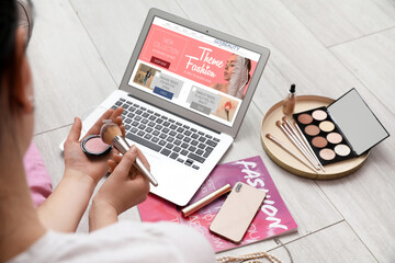 Female beauty blogger with decorative cosmetics, laptop and accessories on light wooden floor
