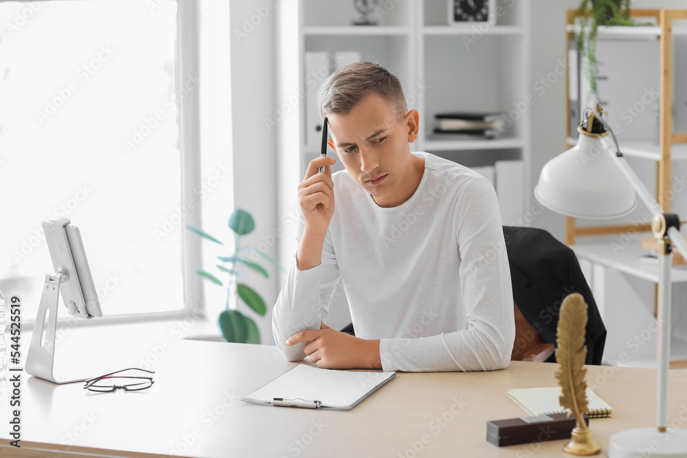 Thoughtful young man with pen sitting at table in office