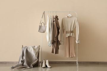 Wall Mural - Rack with warm female clothes and bag near color background
