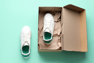 Cardboard box with white sneakers on color background