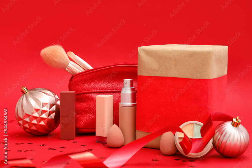 Makeup products with cosmetic bag, gift and Christmas decor on red background