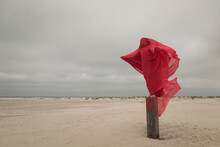 Abstract Portrait Of Woman In Red Thin Fabric On Beach Pole Near Ocean On Windy Cloudy Day