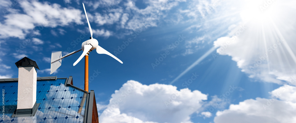 Solar panels and a small wind turbine on the top of a roof of a house ...