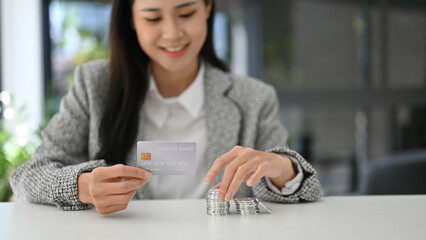 Sticker - Attractive Asian female holding a credit card, stack of silver coins on the table. finance, banking