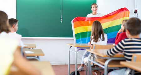 Wall Mural - Teacher explaining meaning of LGBT flag to kids in classroom during lesson in school.