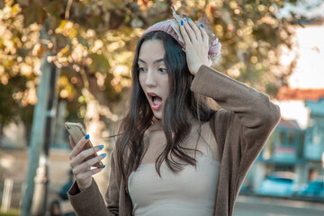 Wall Mural - young woman with surprise gesture and mobile phone on autumn background