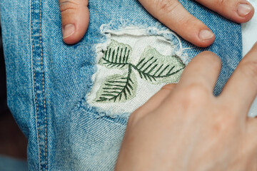 A woman mends jeans, sews a patch on a hole, hands close-up.Mending clothes concept,reusing old jeans.
