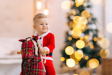 little boy sits on rocking horse and smile. blurred Christmas tr