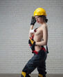 sexy girl with bare breasts in a construction helmet and clothes with a paint roller in her hands