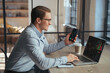 © Arsenii - Smiling businessman crypto trader holding smartphone checking candlestick graph on laptop, buying and selling currency, happy to notice tendency of btc rising up, golden bitcoin near on table