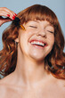 © Jacob Lund - Smiling woman applying face serum with a dropper in a studio