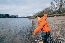 African American Little Kid Play Throwing Stones Into The Water Lake In A Cold Day