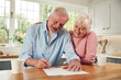 © Monkey Business - Retired Senior Couple Sitting In Kitchen At Home Signing Financial Document