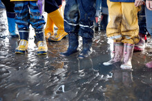 Children's Feet In Rubber Boots, Mudflat Hike At Low Tide On The North Sea, Close Up.