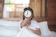 © BoszyArtis - Asia woman holding alarm clock on white bed.