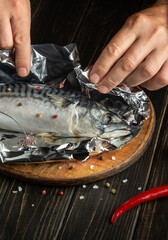 The chef hands preparing mackerel in the kitchen. Wrapping fish in foil before baking in the oven