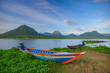 A fishing boat anchored on the edge of the Jatiluhur reservoir with a beautiful mountain scenery in the background