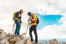Couple Of Hikers Equipped With Backpacks And Trekking Poles Doing High Mountain Route With Their Dog. Mountaineers Climbing A Mountain Peak With Their Pet. Outdoor Activities.