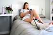 © Cavan Images - Young woman with broken leg lying on bed while using smartphone