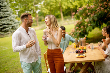 Group of happy young people cheering with fresh lemonade and eating fruits in the garden