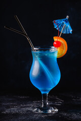 Wall Mural - Glass of blue lagoon cocktail decorated with orange and cherry at festive bar counter background.