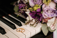 Golden Wedding Rings On The Piano Keys Against The Background Of Flowers