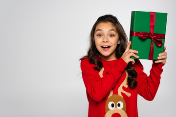 Wall Mural - amazed girl in red sweater holding wrapped Christmas present isolated on grey