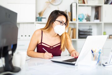 Young colombian woman in mask working with laptop at the office table