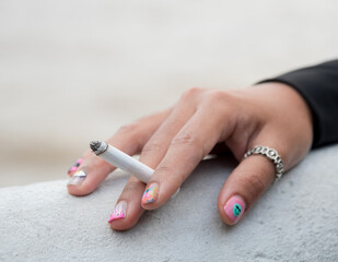 Closeup hand woman teen young asia one person wearing a black shirt hold smoking cigarette white color standing outdoor by the wall 