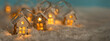 Leinwandbild Motiv Abstract Christmas Winter Panorama with Wooden Houses Christmas String Lights in Cold Snow Landscape and Glowing Golden Lights in Background. Panorama, Banner. Christmas or Energy themes.