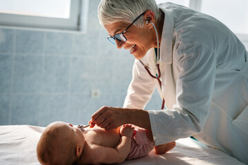 Wall Mural - Happy pediatrician doctor with baby checking possible heart defect